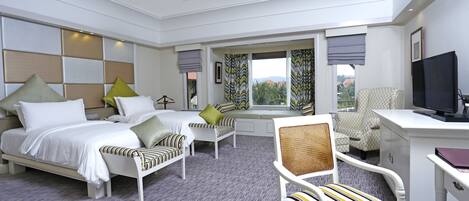 A hotel room with a bed, two bedside tables, a desk, a chair, a television, and a window with curtains.