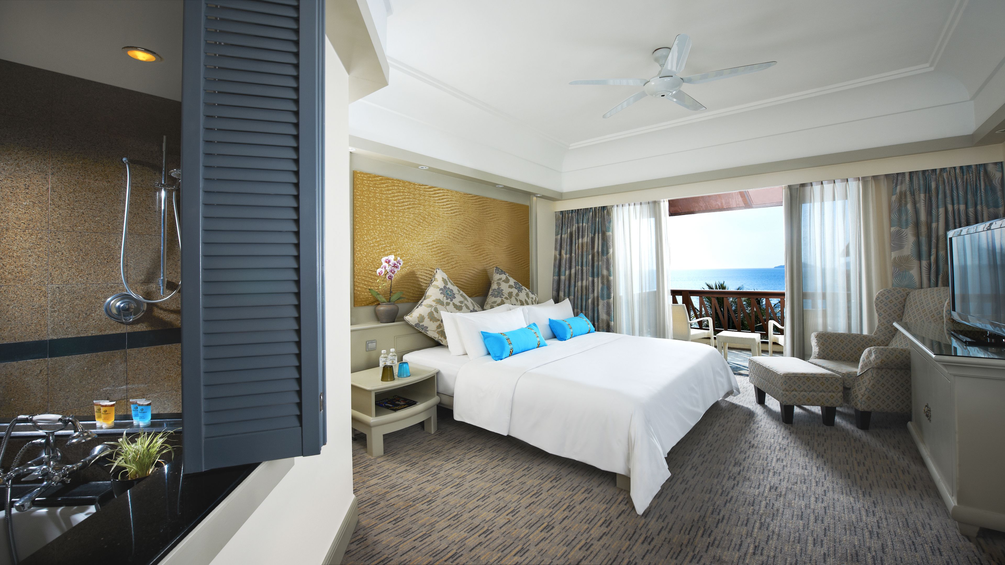A hotel room with a bed, a TV, a balcony with a view, a shower, and a ceiling fan.
