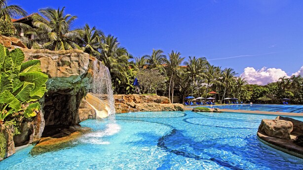 A pool with a waterfall feature surrounded by palm trees and a clear blue sky. - The Magellan Sutera Resort (Kota Kinabalu)