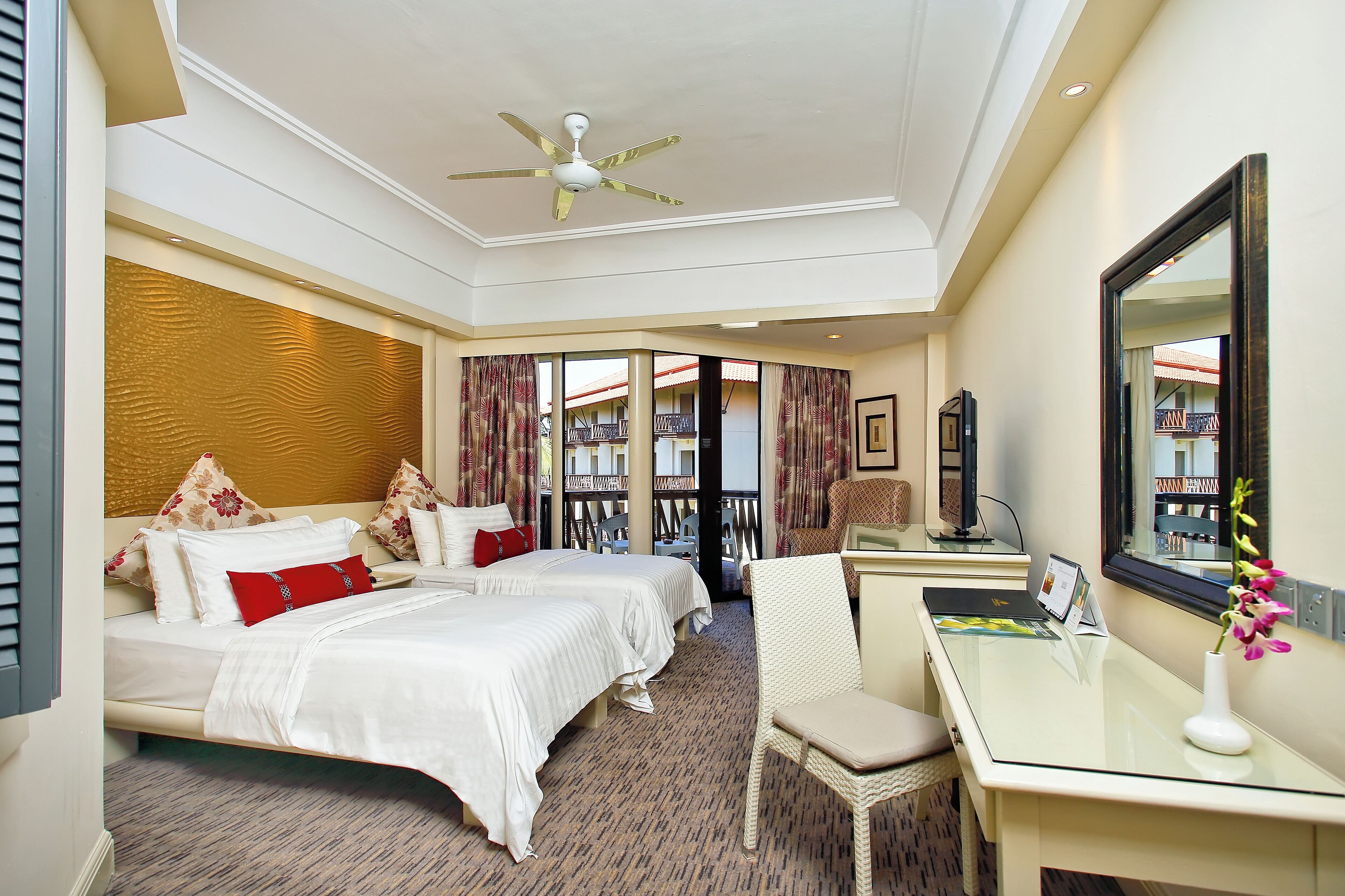 A hotel room with two beds, a desk, a chair, a large mirror, and a ceiling fan.