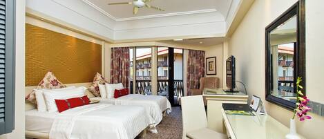 A hotel room with two beds, a desk, a chair, a large mirror, and a ceiling fan.