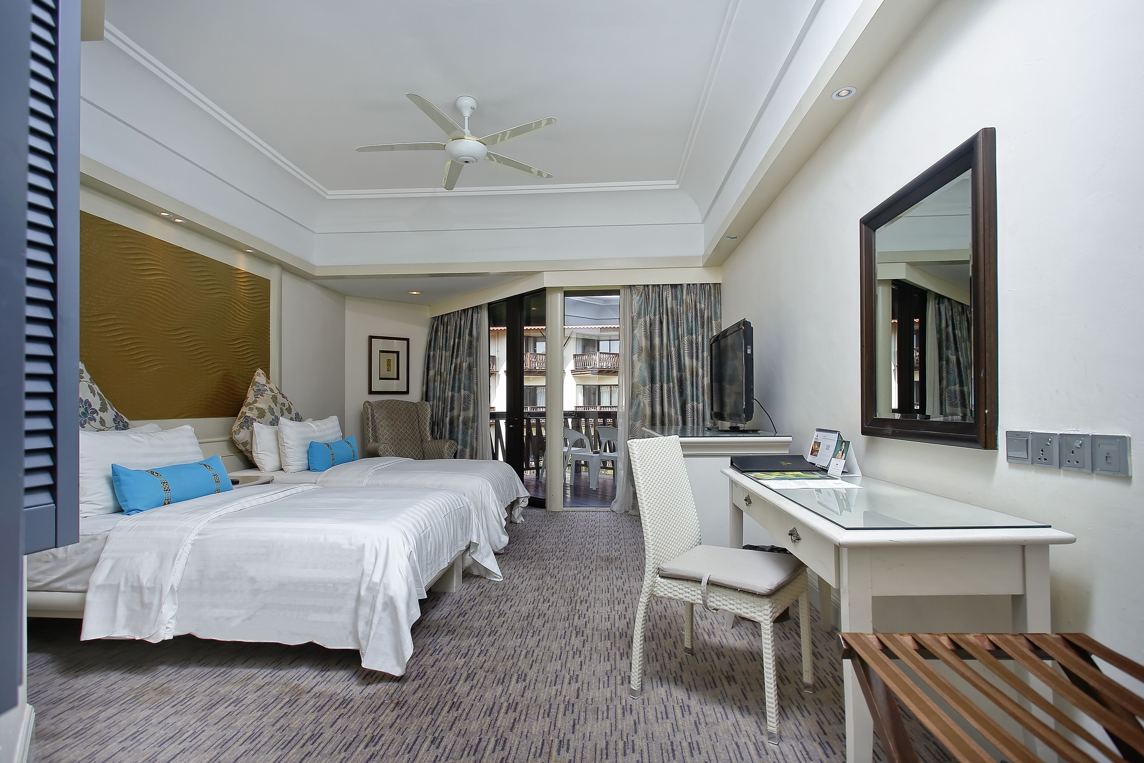 A hotel room with a bed, a desk, a chair, a TV, and a balcony with curtains.
