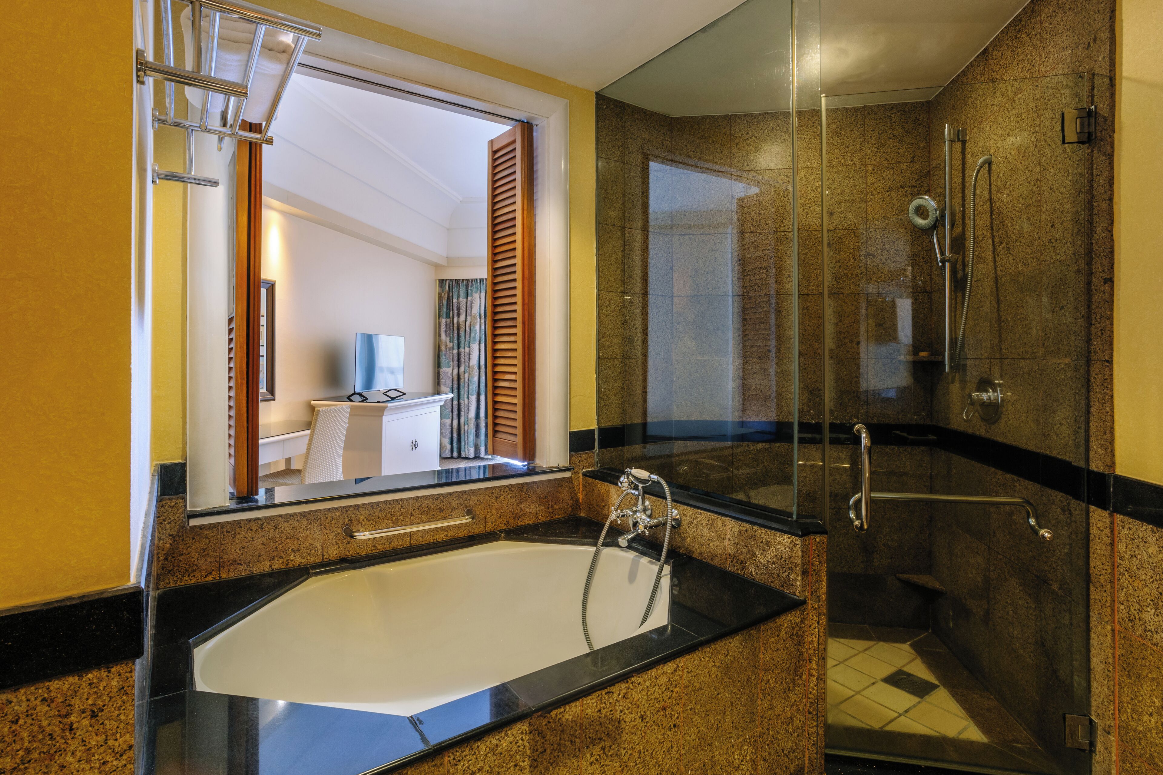 Un baño moderno con una bañera grande, una ducha con mampara de vidrio y un espejo que refleja un cuarto con escritorio y cortinas.
