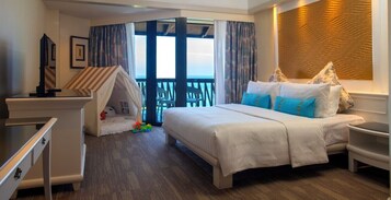 A hotel room with a bed, a desk, a chair, a small play area, and a balcony with a view.