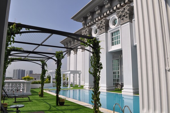 Zona de piscina con pérgola, columnas blancas y vista a rascacielos.