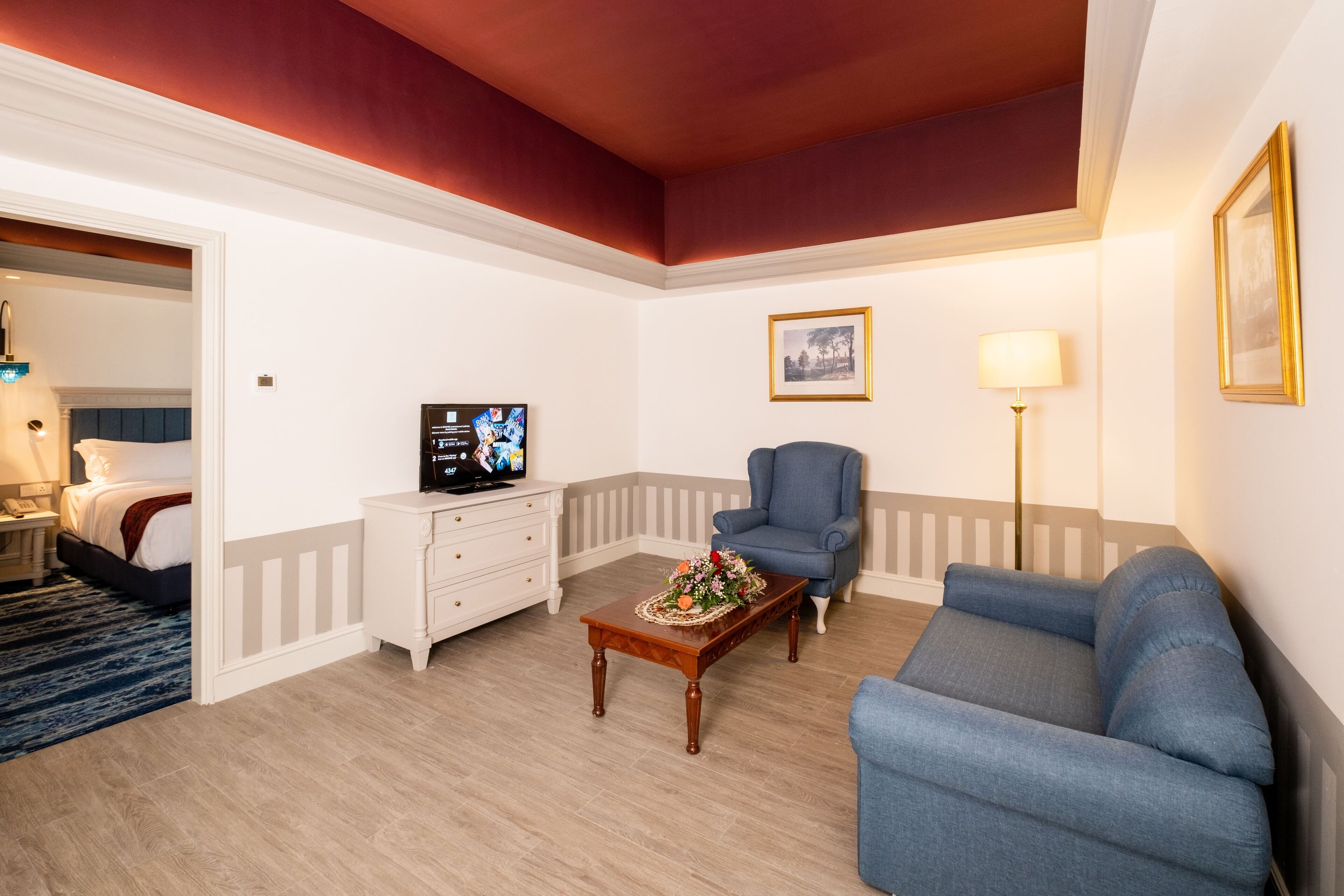 Un salon avec un canapé bleu, une table basse en bois agrémentée d’un arrangement floral, un fauteuil bleu, une commode blanche et un téléviseur posé sur un meuble.