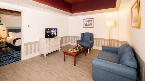 A living room with a blue sofa, a wooden coffee table with a floral centerpiece, a blue armchair, a white dresser, and a television on a stand. - Grand Swiss-Belhotel Melaka (Malacca City)