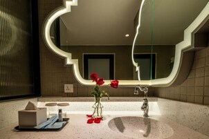 Un baño moderno con un diseño de espejo único, un lavabo y un florero con rosas rojas.