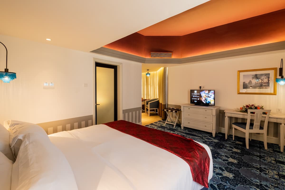 Habitación de hotel con una cama grande, un escritorio, una silla, un televisor y un cuadro en la pared.