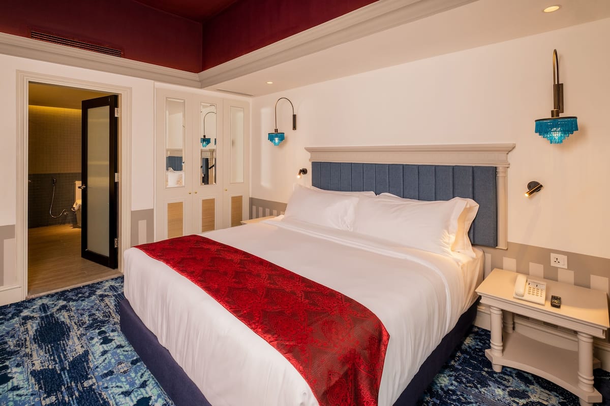 Habitación de hotel con una cama grande, una mesita de noche con teléfono y un baño visible a través de una puerta abierta.