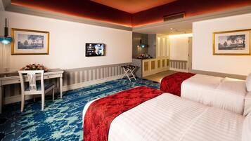Habitación de hotel con dos camas, un escritorio, una silla, un televisor y obras de arte en las paredes.