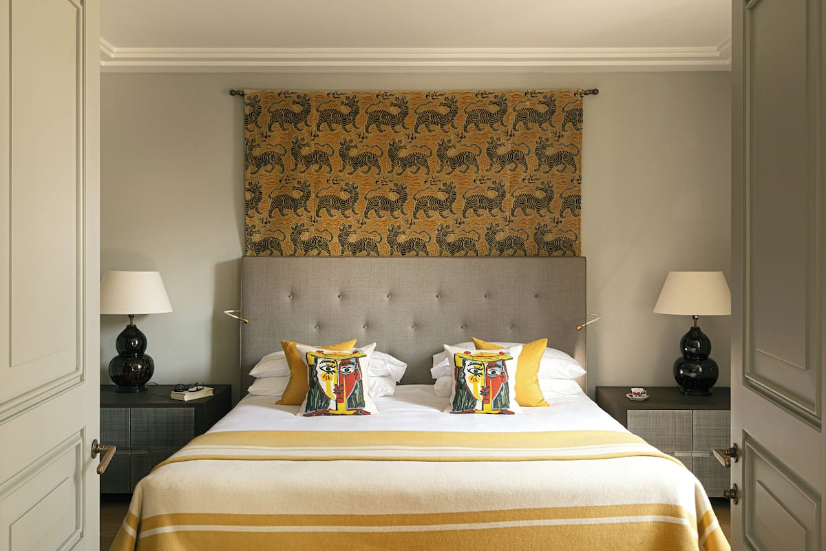 A hotel room with a large bed, two nightstands, a headboard with a tapestry, and two lamps.