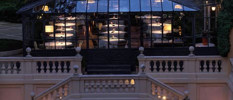 Un edificio lujoso con estructura de techo de vidrio, balcones ornamentados y una gran escalera que conduce a una entrada.
