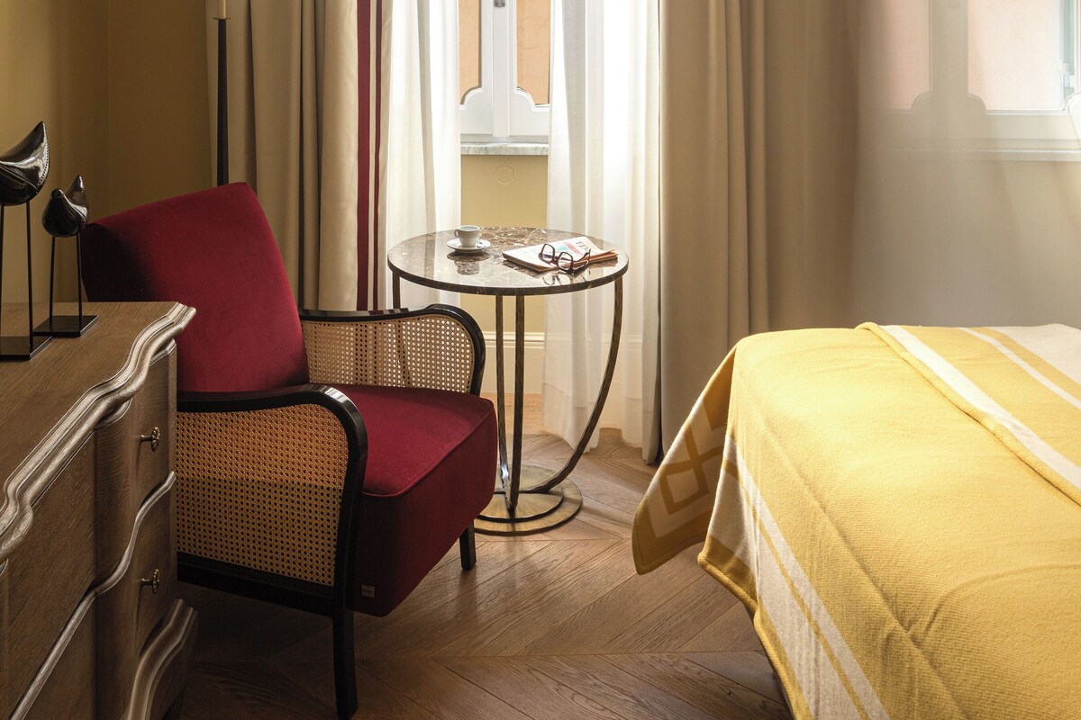 Una habitación de hotel con una cama, una silla, una mesa y una taza, además de cortinas.
