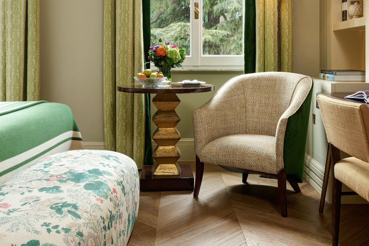 A hotel room with a bed, a chair, a table with a lamp, and a window with curtains.