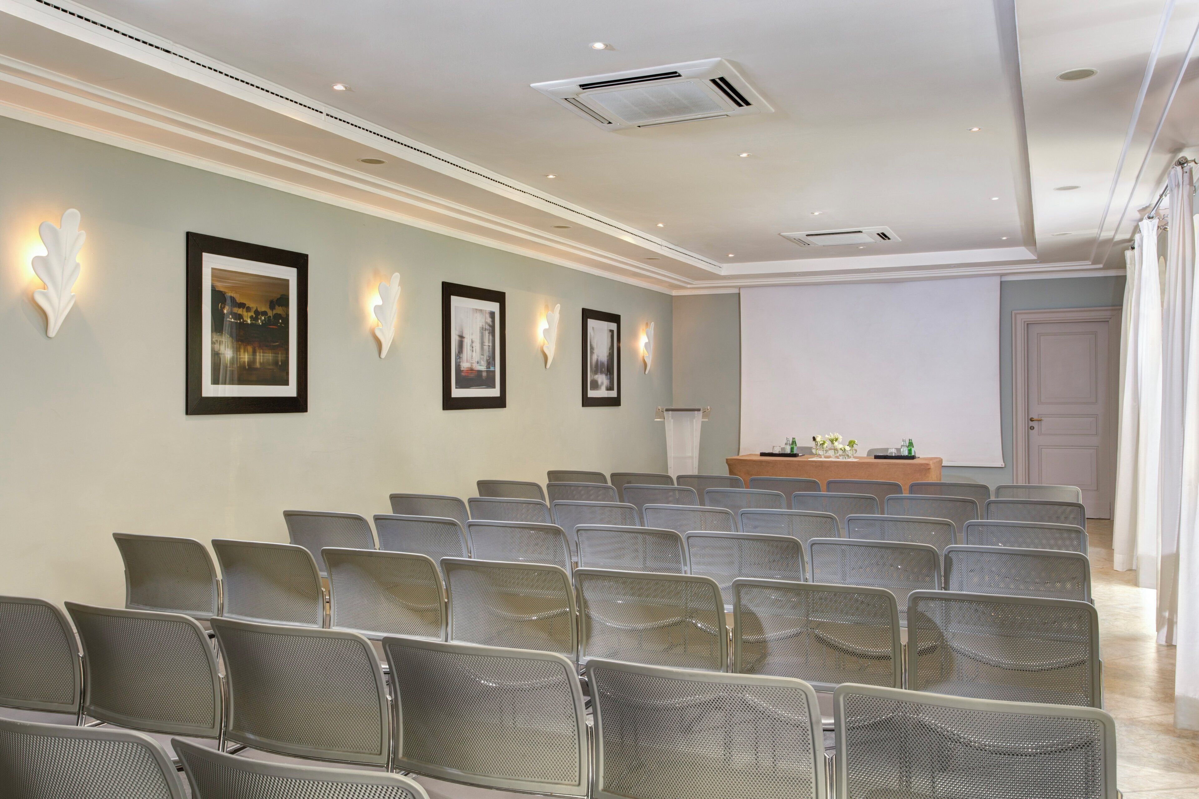 A conference room with rows of chairs, a podium, and framed pictures on the wall.