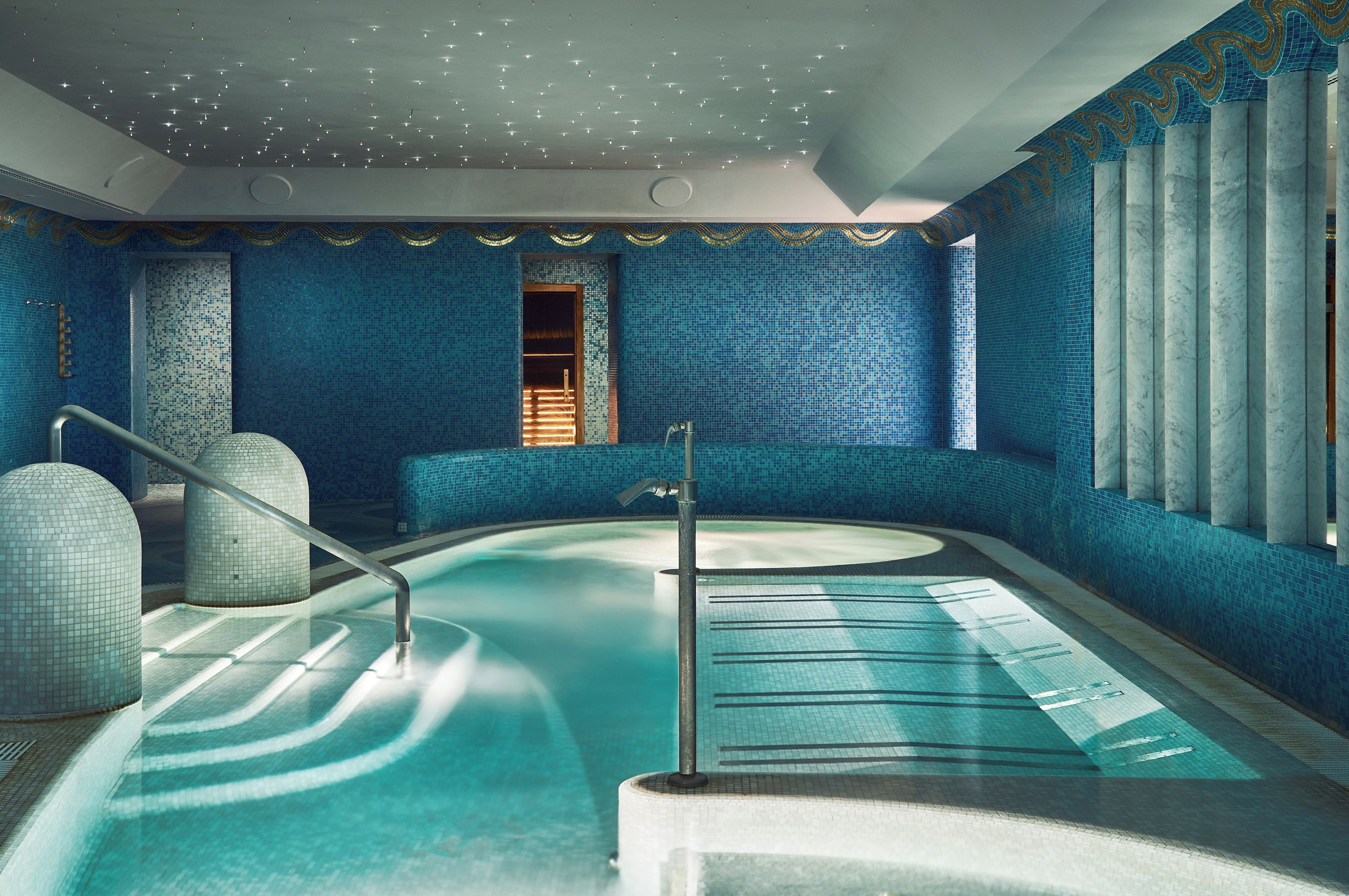 Una amplia piscina interior con diseño curvo, rodeada de paredes con azulejos azules y un techo decorativo.