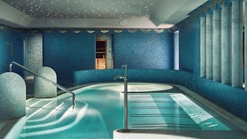 Una amplia piscina interior con diseño curvo, rodeada de paredes con azulejos azules y un techo decorativo.