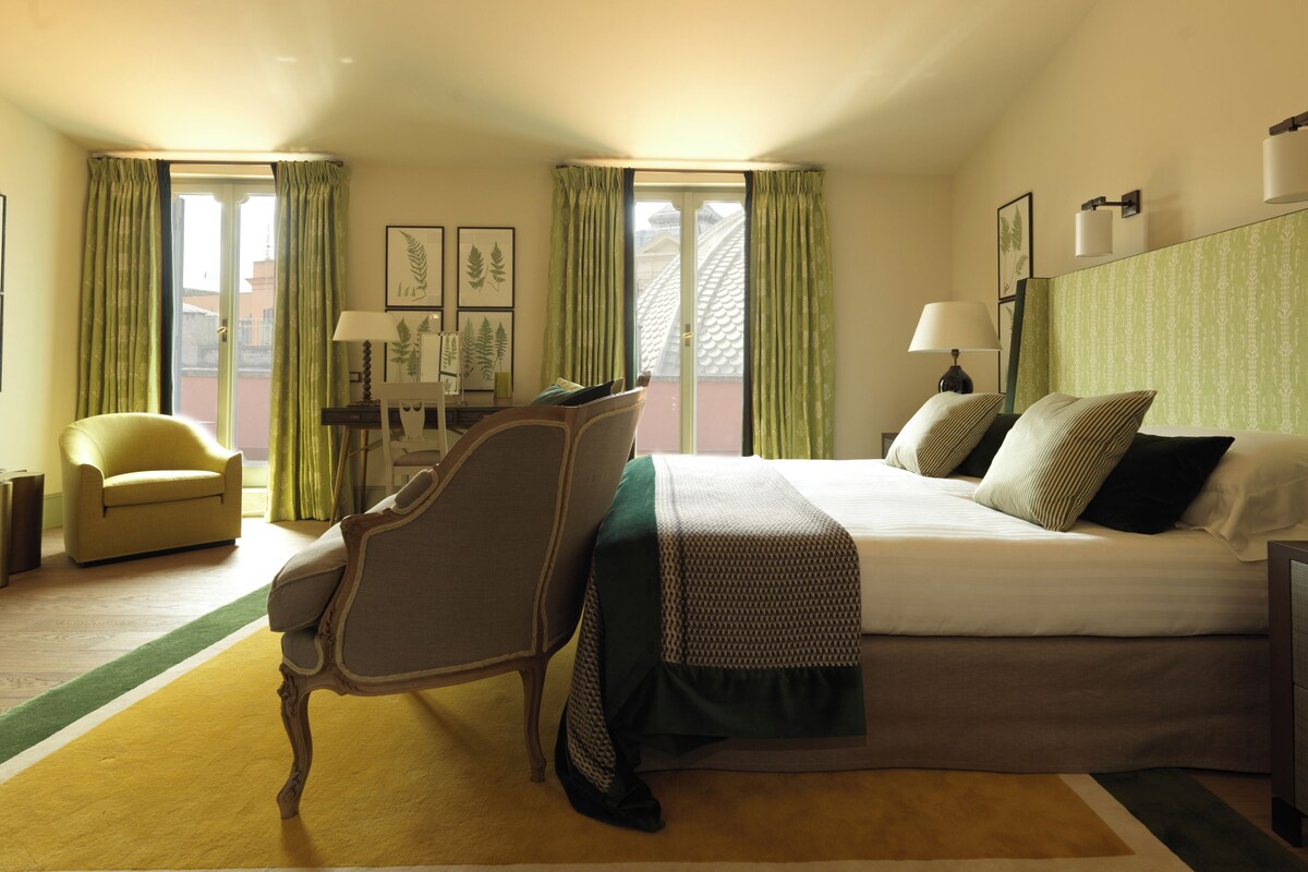 Una habitación de hotel con cama, escritorio, silla y ventana con cortinas.