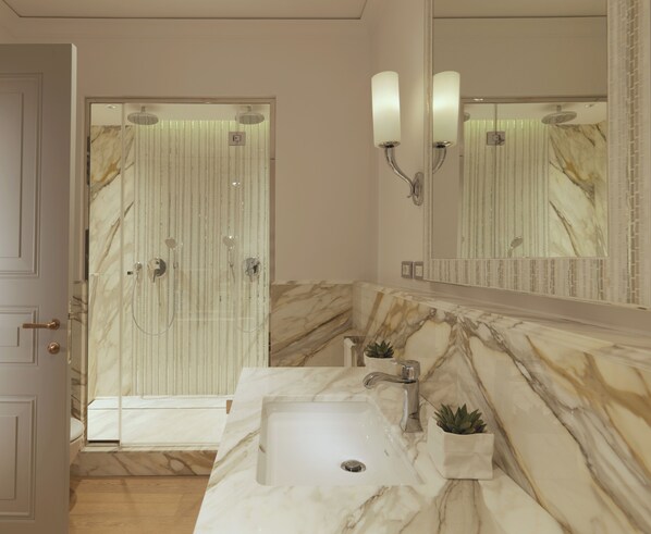 A bathroom with a marble vanity, a sink, a mirror, and a shower with a glass door.