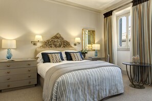 A hotel room with a bed, bedside tables, lamps, a mirror, curtains, and a small round table with a vase. - Rocco Forte Hotel De Russie (Rome)