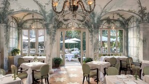 A restaurant with tables set for dining, a chandelier, and a view of the outdoor seating area. - Rocco Forte Hotel De Russie (Rome)