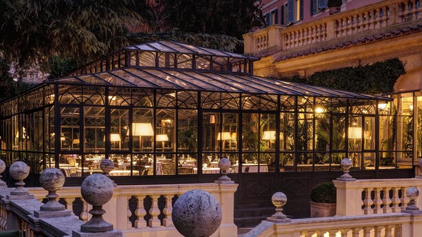 A glass-roofed conservatory with tables and chairs, surrounded by a balustrade with spherical finials. - Rocco Forte Hotel De Russie (Rome)