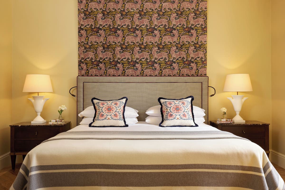 A hotel room with a large bed, two nightstands, and a patterned tapestry above the bed.