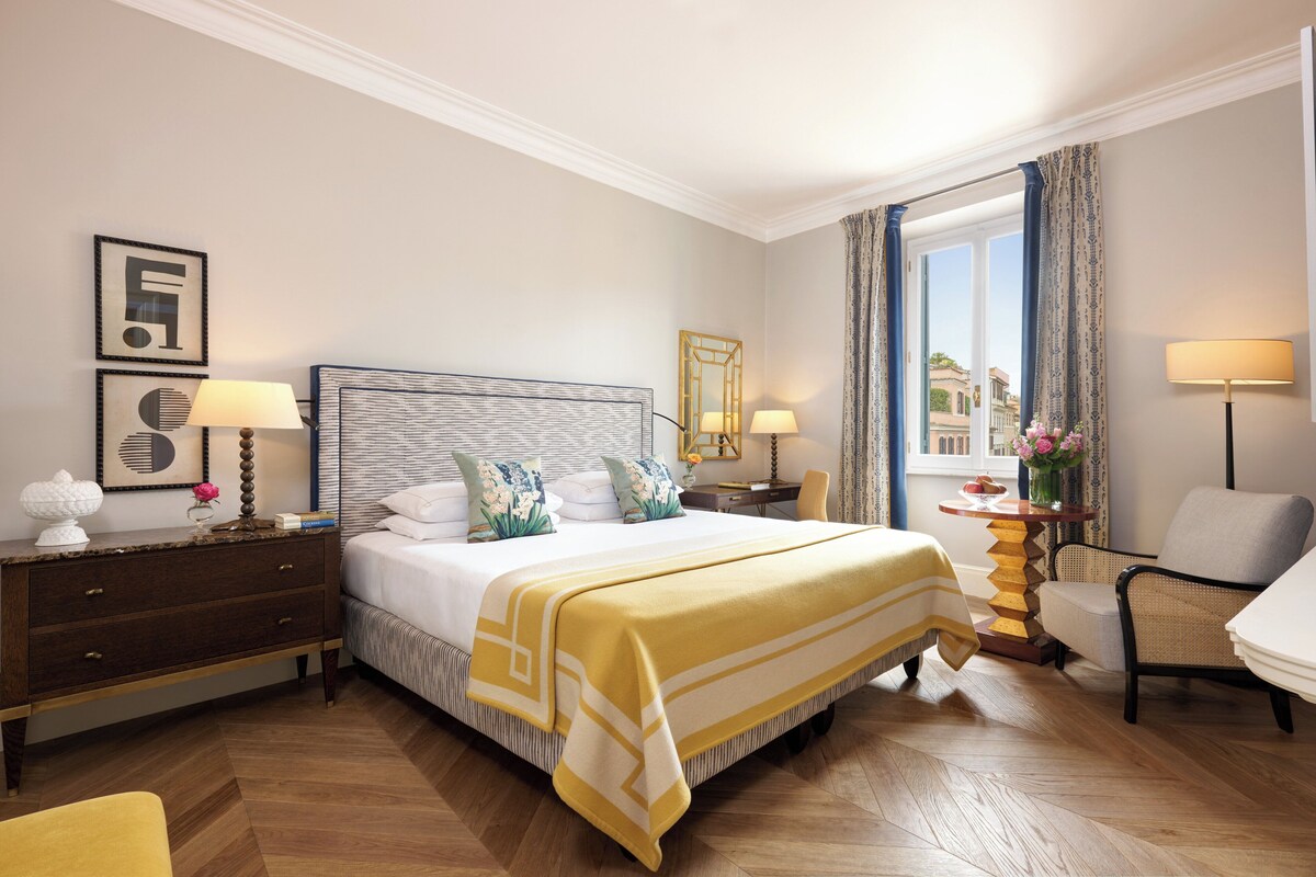 Habitación de hotel con una cama grande, dos mesitas de noche con lámparas, una silla y vistas a la ciudad desde la ventana.