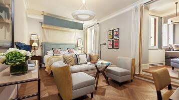 Una camera d'albergo con un letto, un angolo salotto con un tavolo, una libreria e un'ampia finestra con tende.