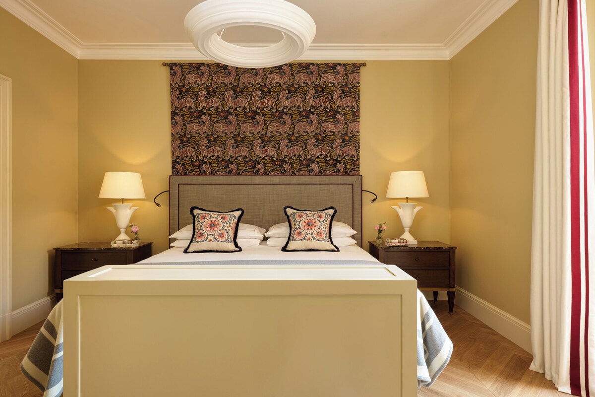 Habitación de hotel con una cama grande, dos mesitas de noche, cabecero y un tapiz en la pared.