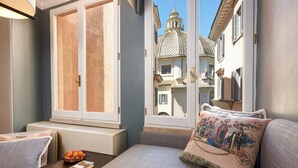 A cozy bedroom with a large window, a bedside table with a fruit bowl, and a decorative pillow. - Rocco Forte Hotel De Russie (Rome)