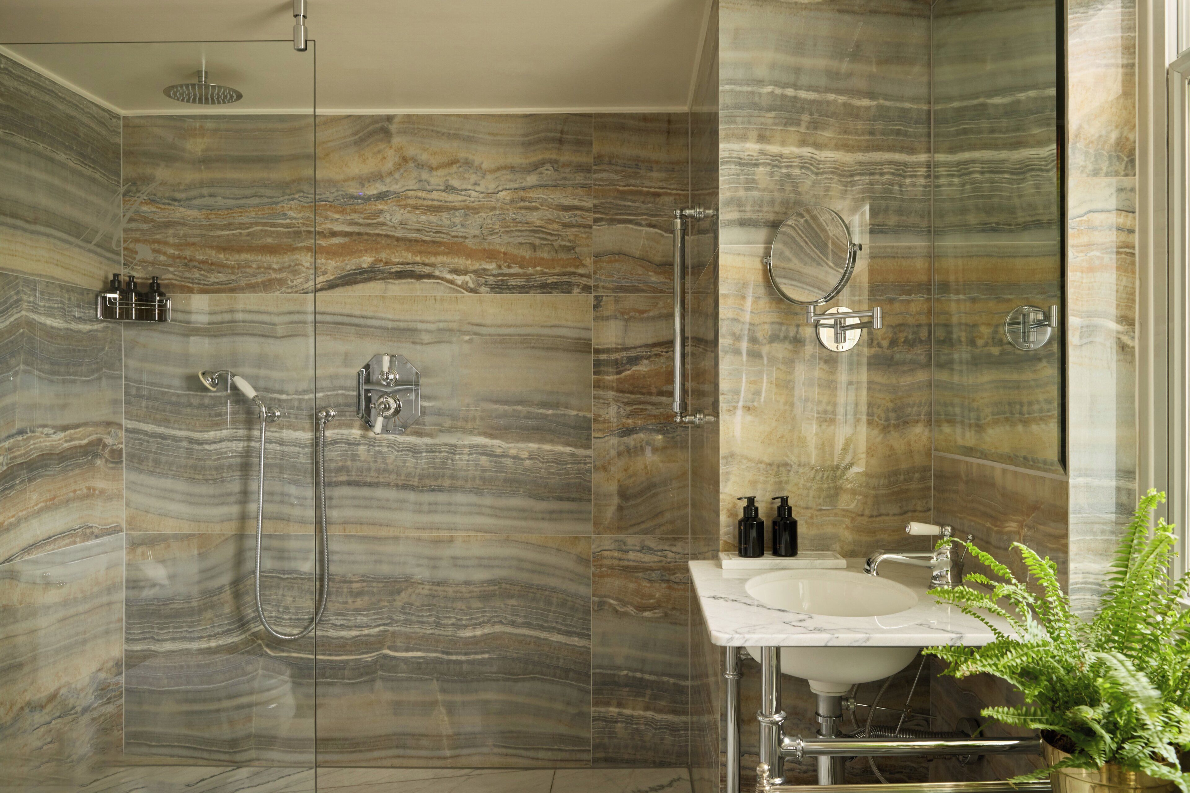 Une salle de bain dotée d’une douche à parois de verre, d’un mur en marbre, d’un lavabo et d’un miroir.