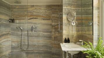 Une salle de bain dotée d’une douche à parois de verre, d’un mur en marbre, d’un lavabo et d’un miroir.