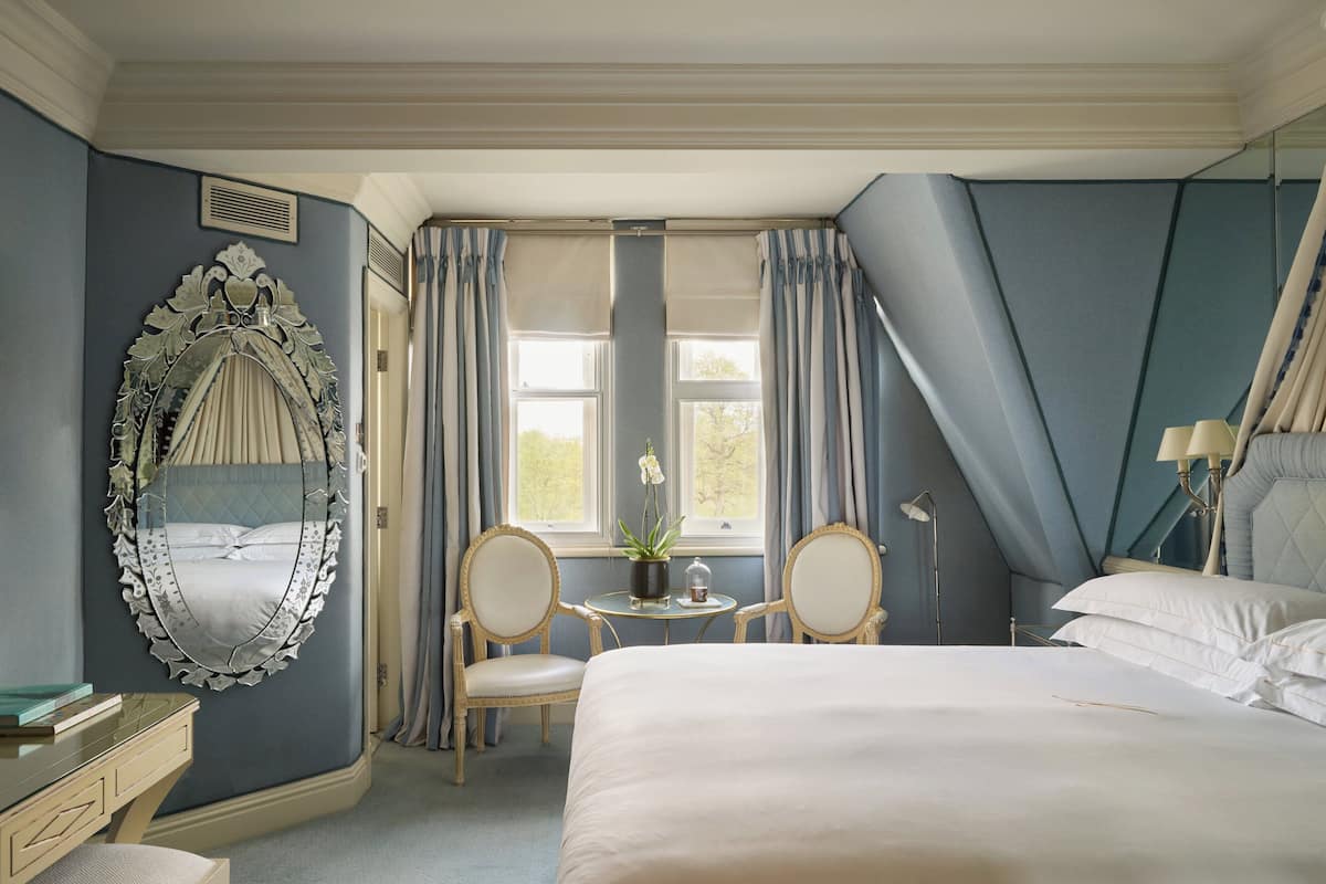 Relax in comfort with a large bed, decorative mirror, and a potted plant, set against a sloped ceiling and large window with a view.
