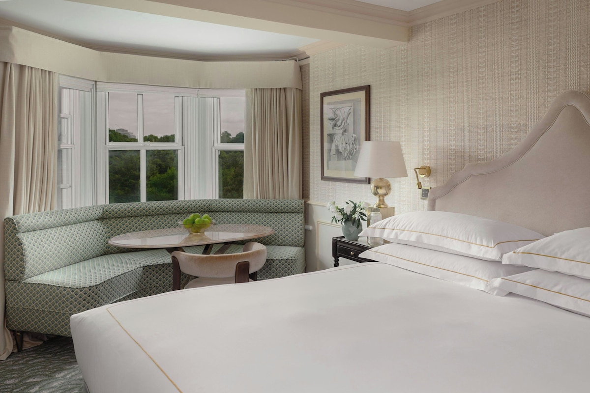 A hotel room with a bed, a sofa, a small table, a lamp, and a window with curtains.