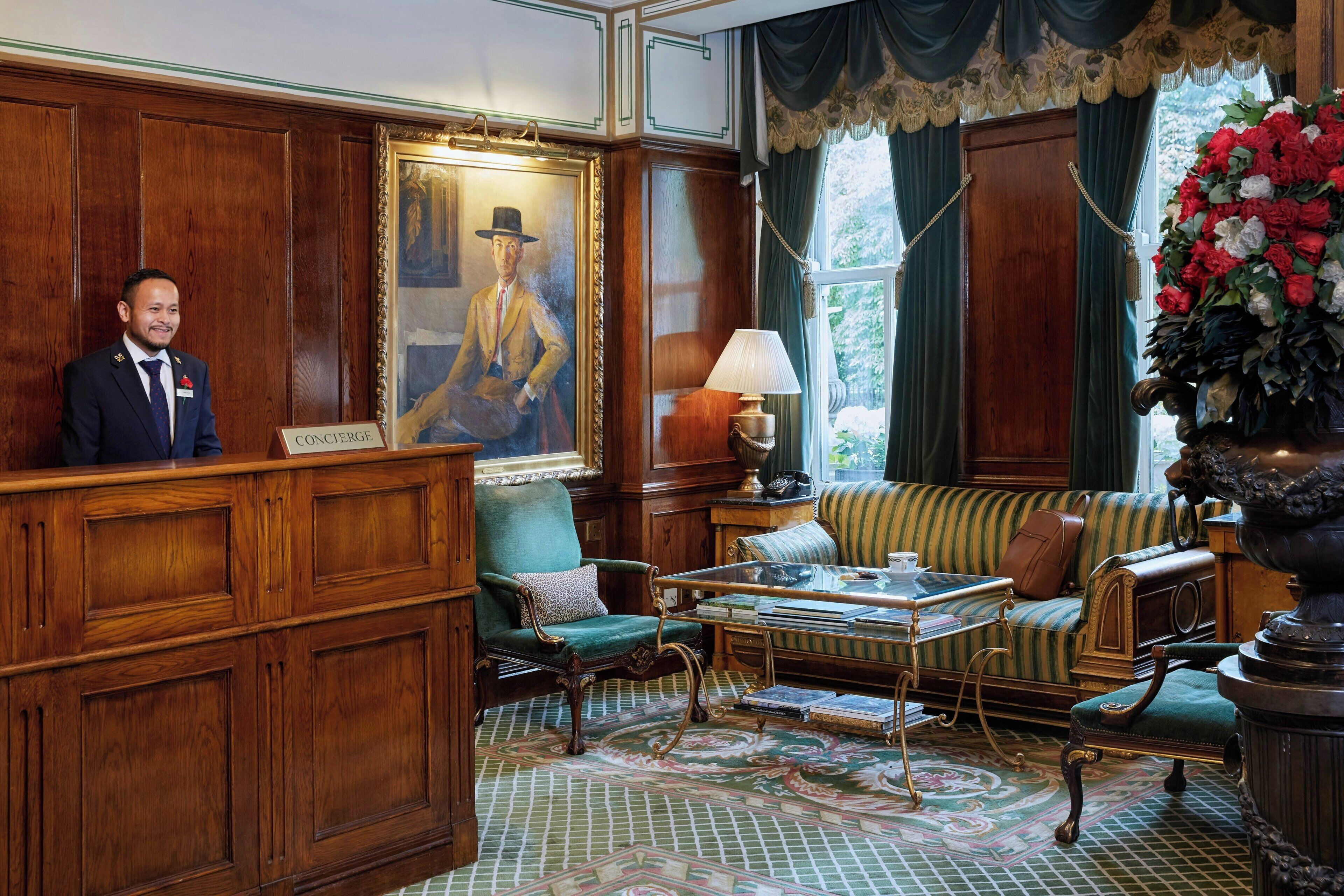 A formal room with a wooden reception desk, a green armchair, a striped sofa, and a large floral arrangement.