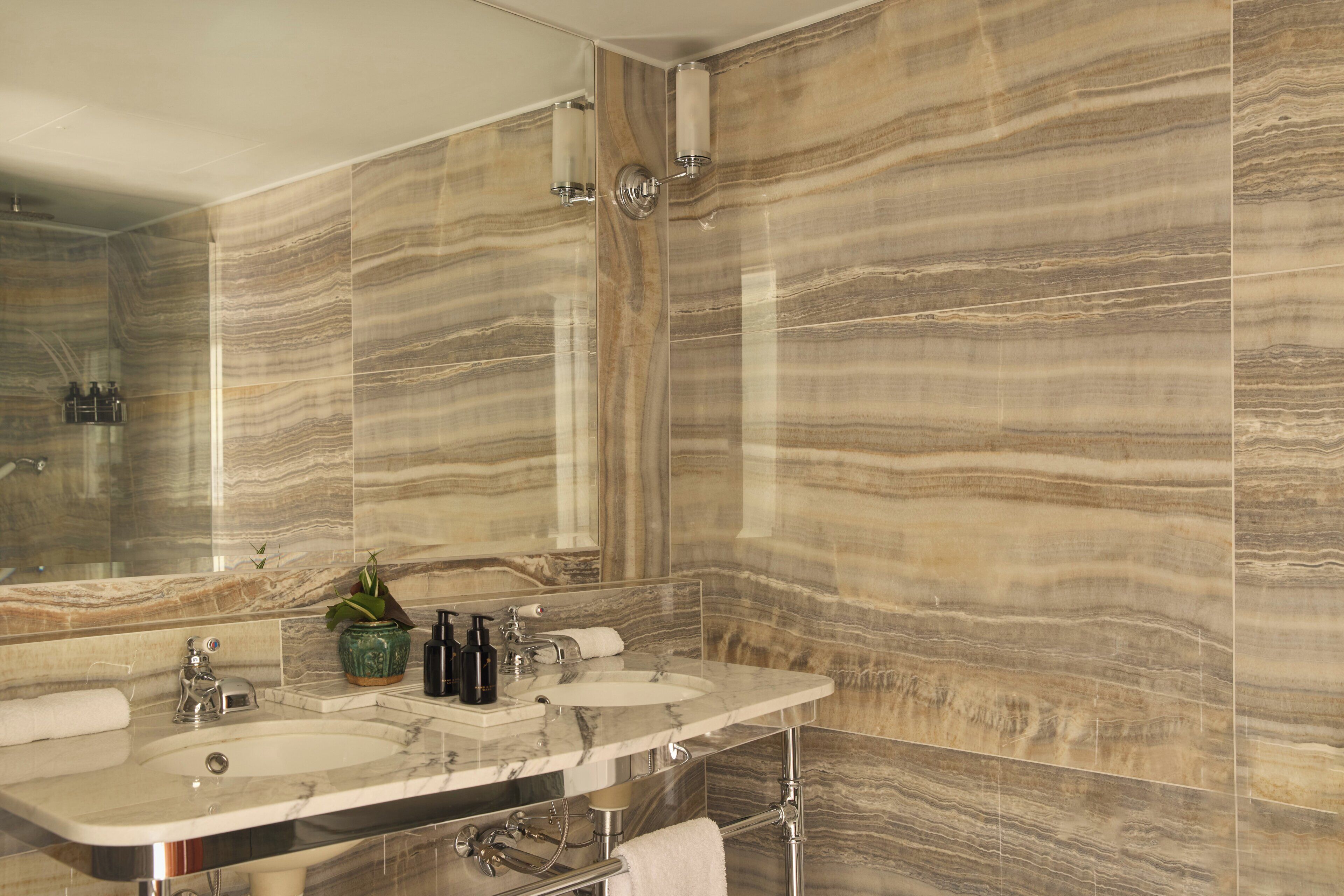 Une salle de bain aux murs recouverts de marbre, dotée d’un double lavabo et d’un grand miroir.