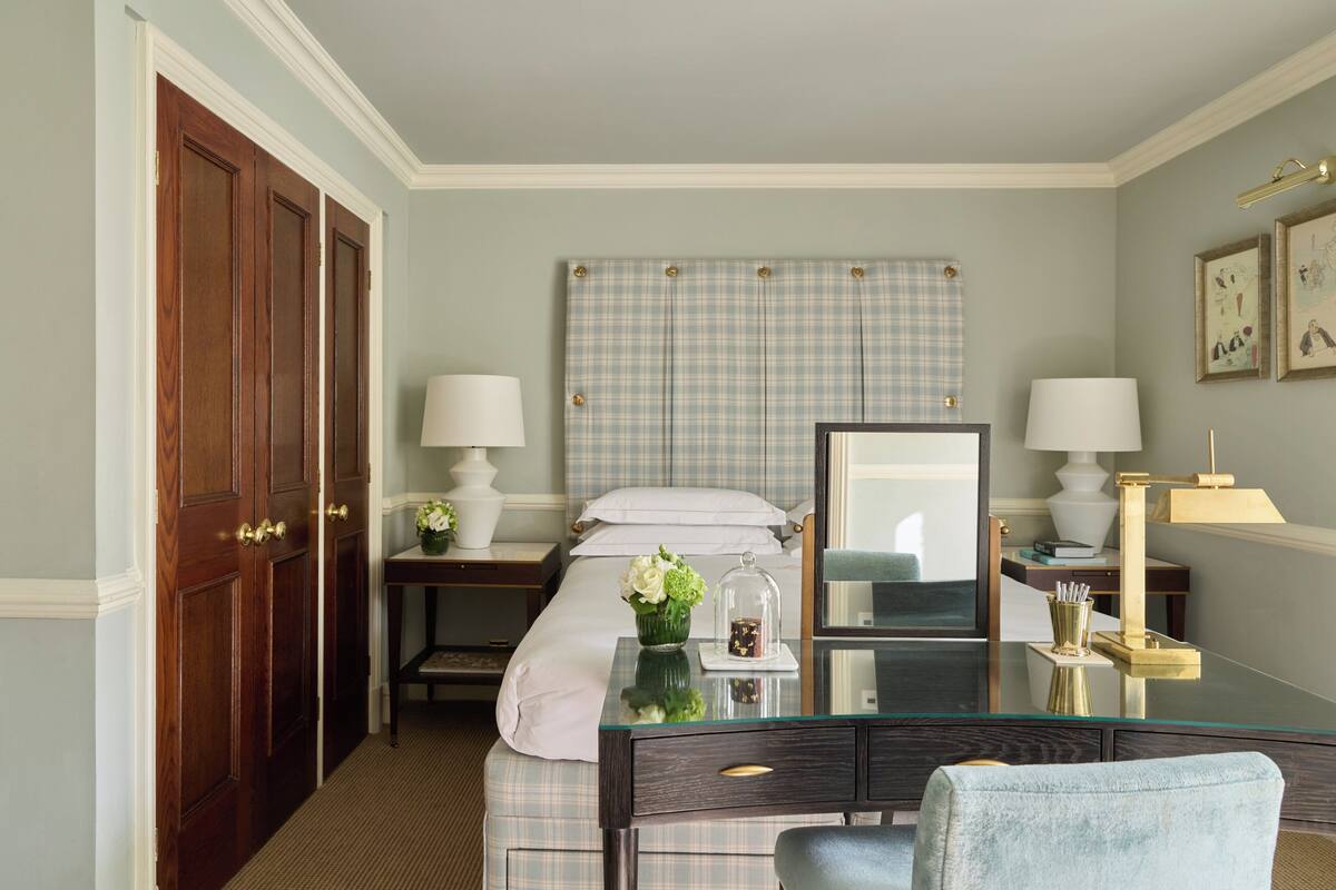 A hotel room with a bed, a desk with a chair, a dresser, and a mirror.