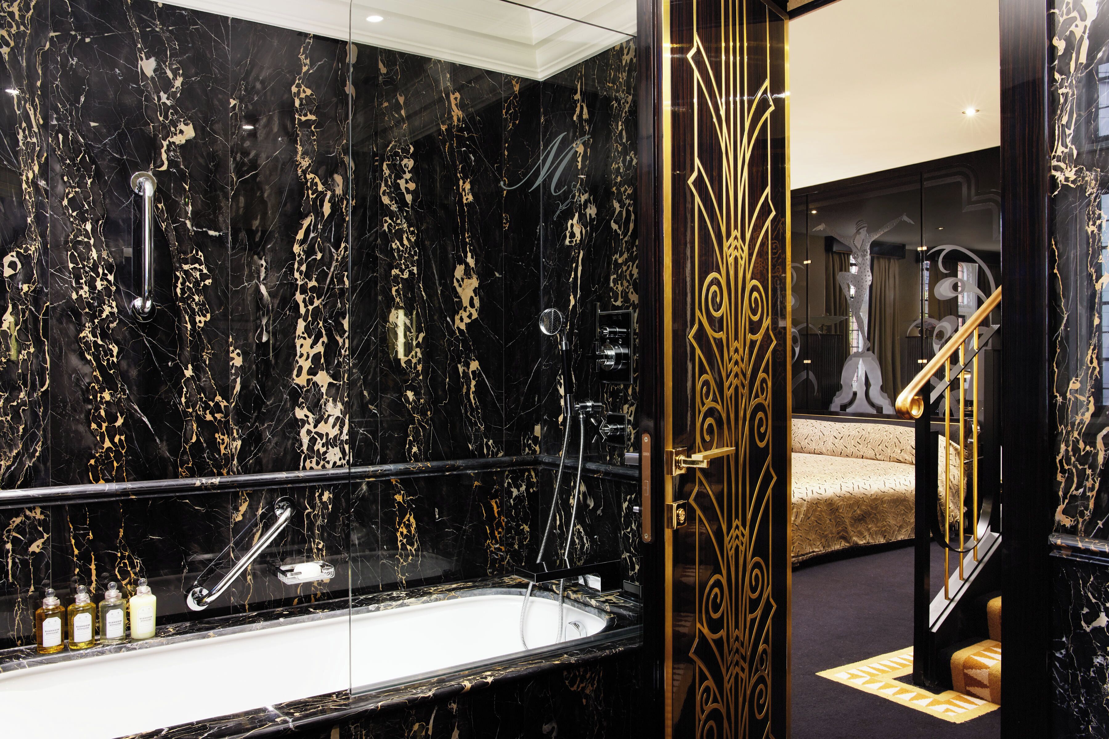 A luxurious bathroom with a black marble sink, a glass-enclosed bathtub, and a gold-framed mirror.