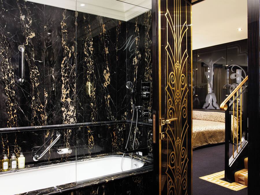A luxurious bathroom with a black marble sink, a glass-enclosed bathtub, and a gold-framed mirror.