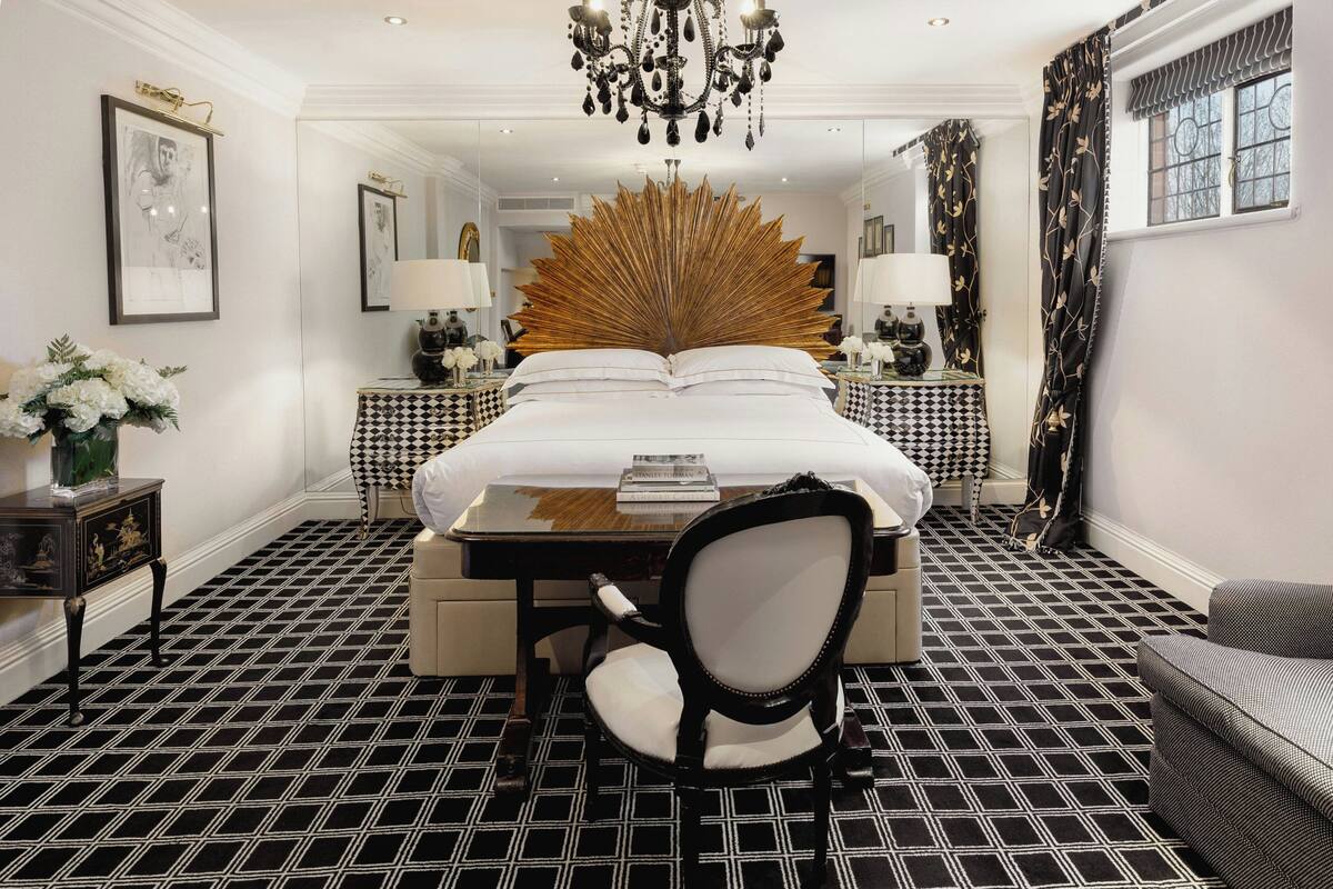 A hotel room with a large bed, a chandelier, a mirror, a desk, and a chair.