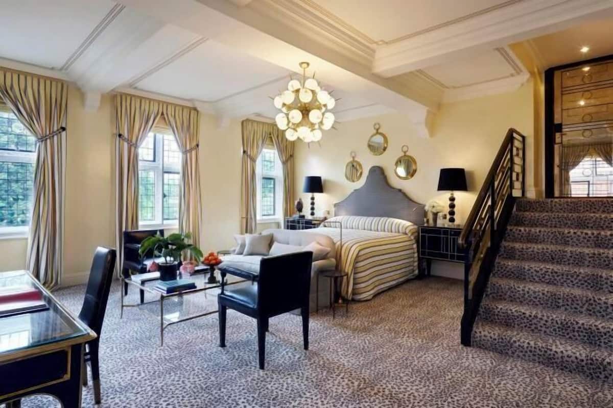 A hotel room with a bed, a desk, a chair, a table, a staircase, and a chandelier.