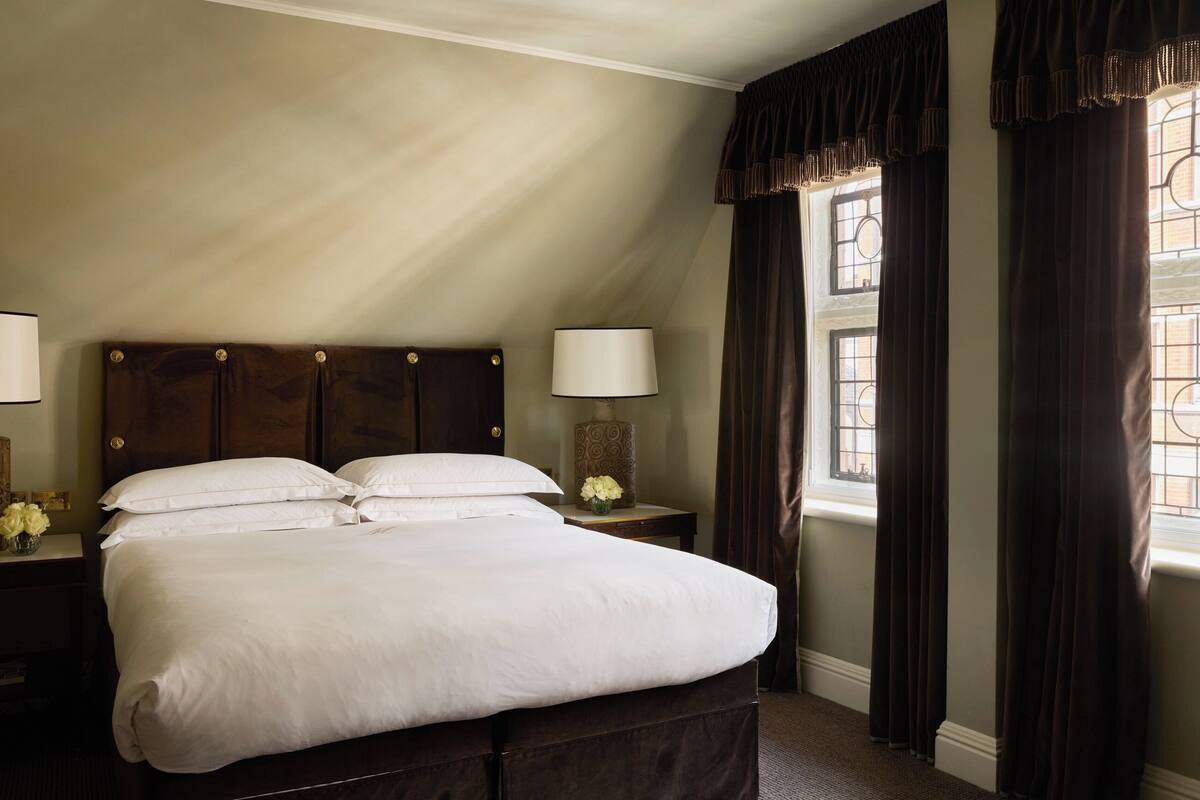 A neatly made double bed with a wooden headboard, a bedside table with a lamp, and a window with curtains.
