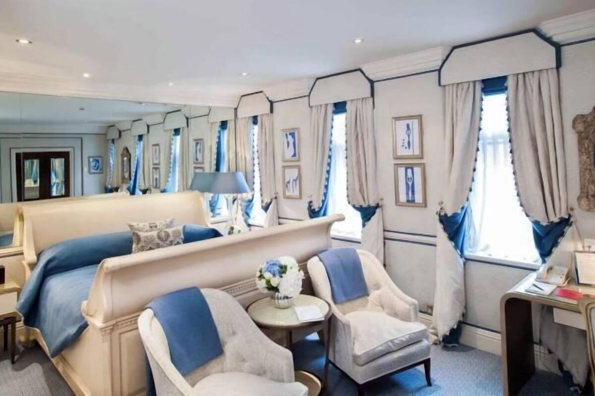 Habitación de hotel con una cama grande, dos sillones, una mesita con un jarrón y un escritorio con una lámpara.