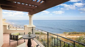A balcony with a view of the ocean, a table with chairs, and a railing.