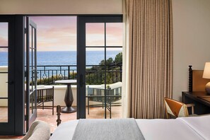 A hotel room with a balcony, a bed, a chair, and a table.