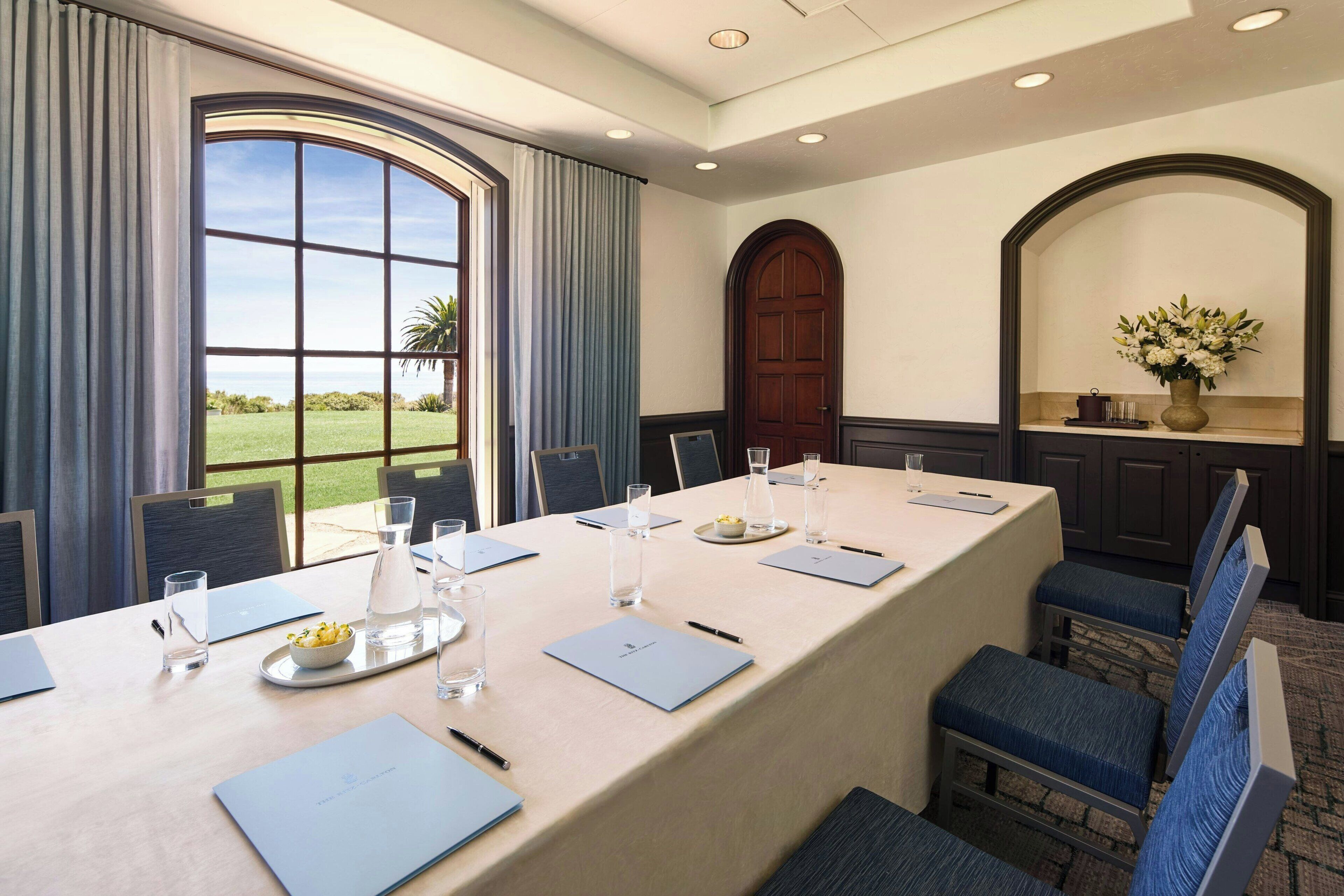 A conference room with a long table, chairs, a large window, and a door.