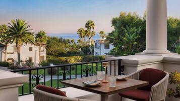 Un balcon avec une table et des chaises, donnant sur un jardin aménagé et offrant une vue sur la mer.