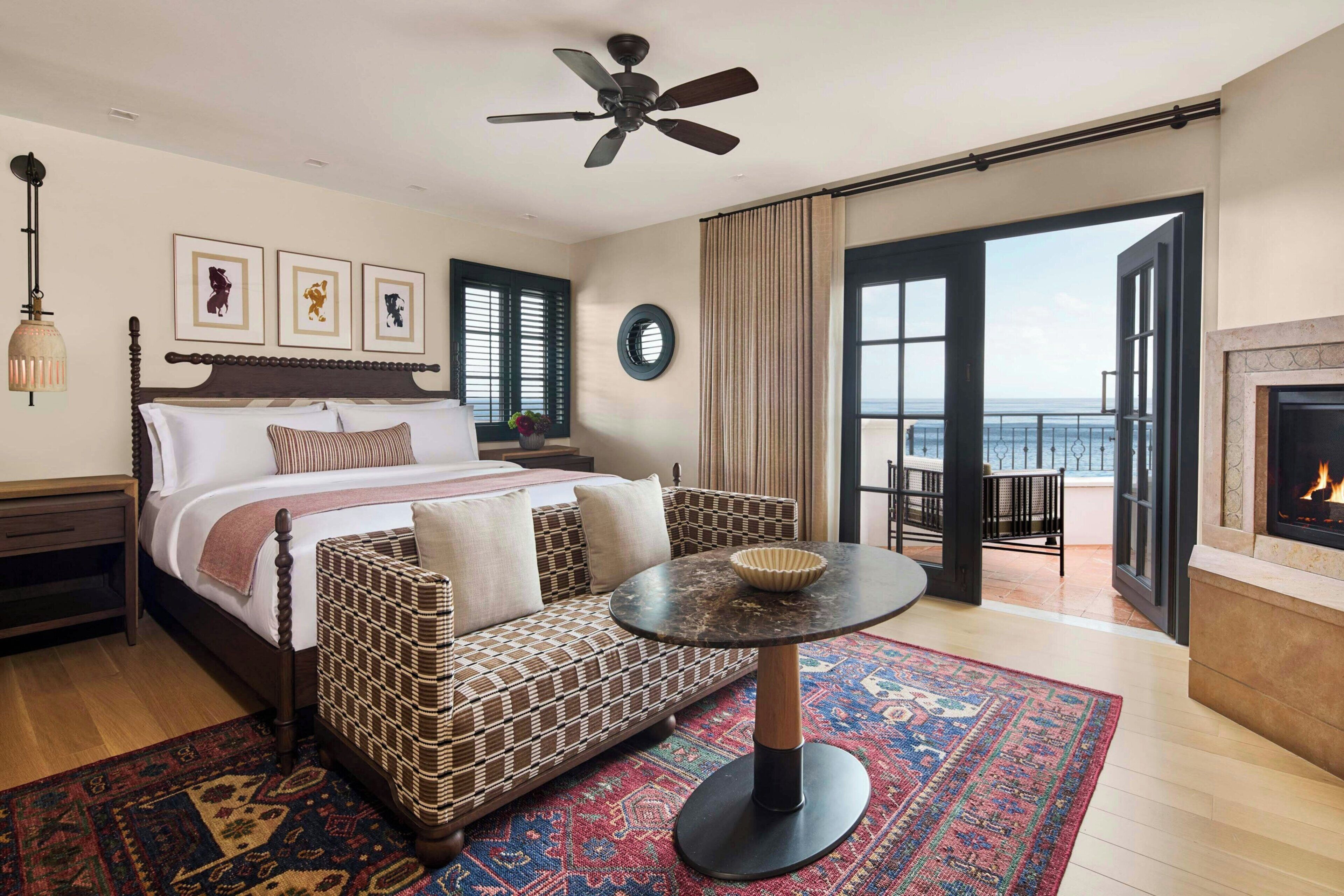 Une chambre à coucher comprenant un lit, un canapé, une table ronde, un ventilateur de plafond, une cheminée et une vue sur la mer.